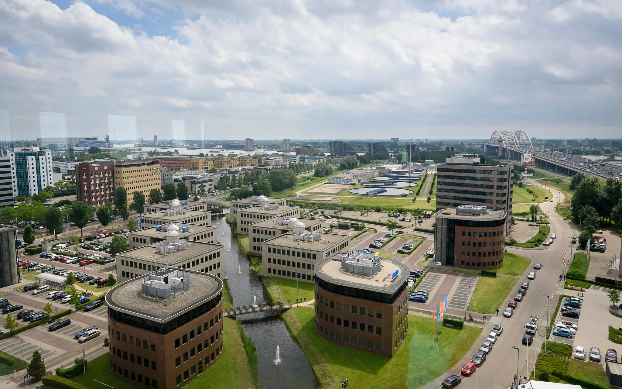 Luchtfoto van het Rivium Quadrant in Capelle aan den IJssel met kantoren, waterpartijen en de Van Brienenoordbrug op de achtergrond.